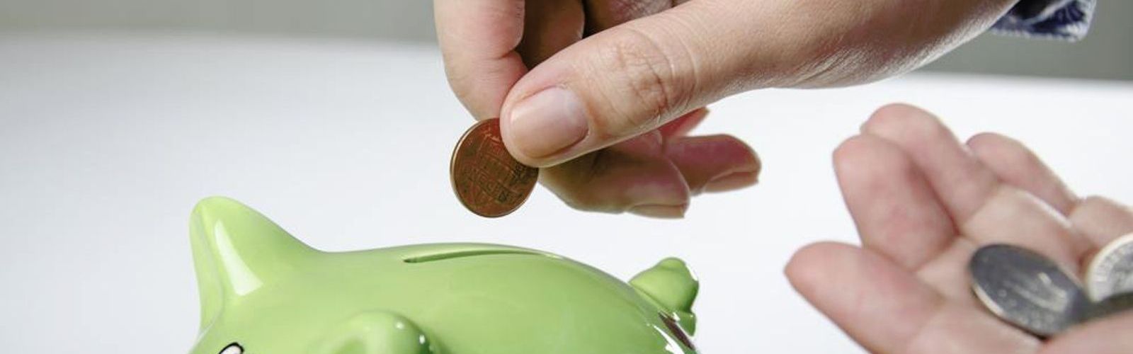 hand putting money into a green piggy bank_131199065_web.jpg