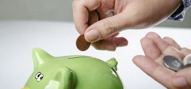 hand putting money into a green piggy bank_131199065_web.jpg