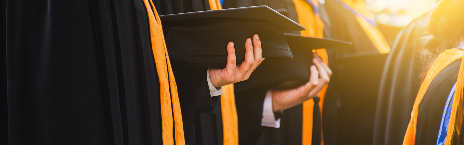 graduates holding mortarboards with bright sun 1600x500px.jpg